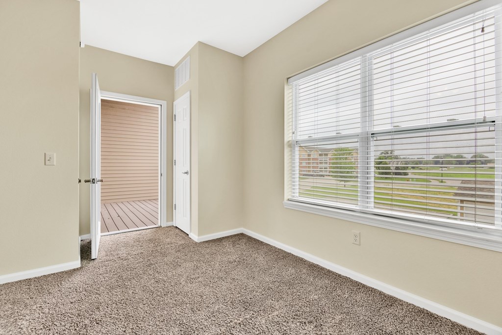 A room with a carpeted floor, a window with blinds, and a door leading to a deck.