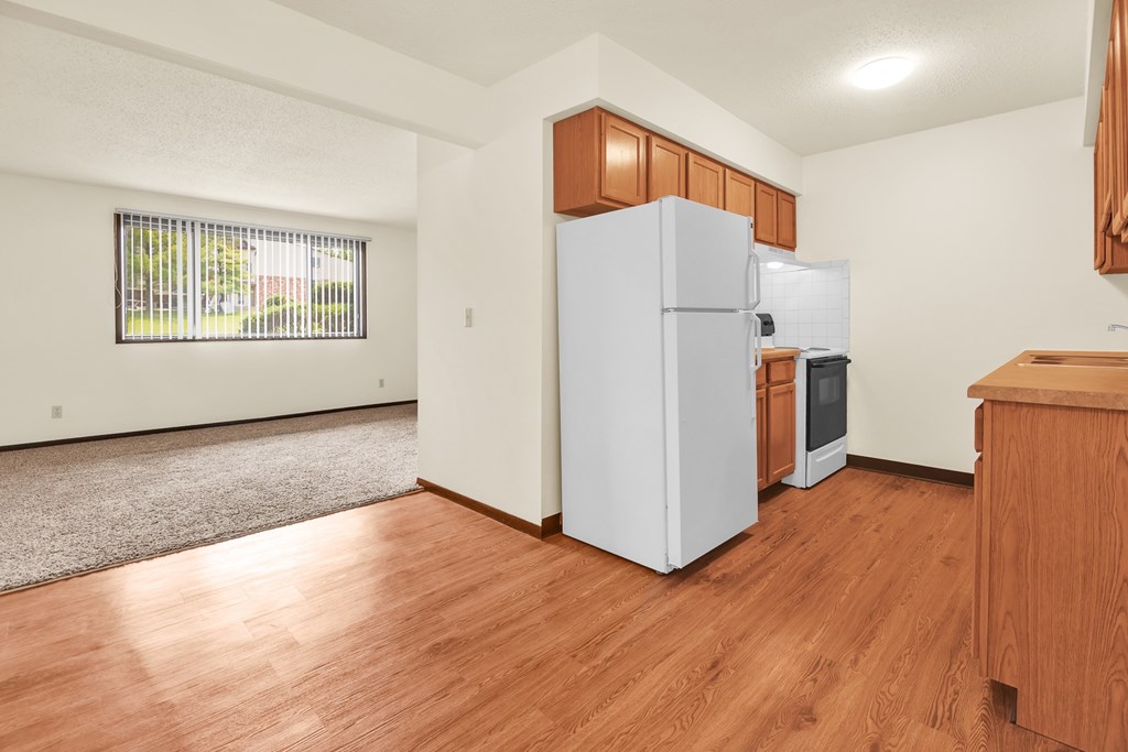 A white refrigerator is in a kitchen with wooden floors and cabinets.