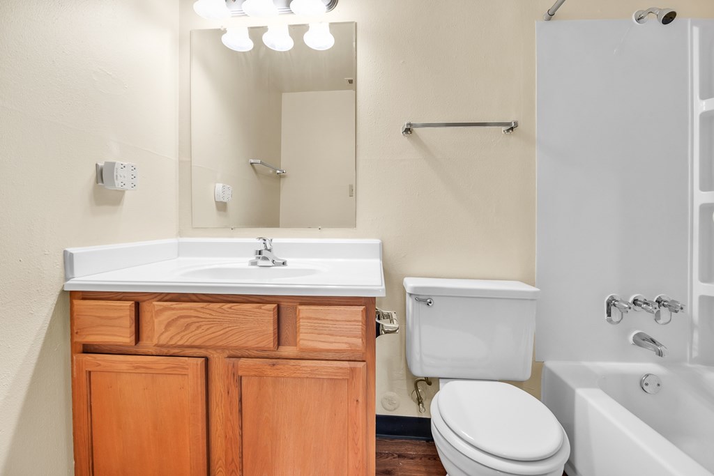 A white sink with a wooden cabinet and a white toilet in a bathroom.