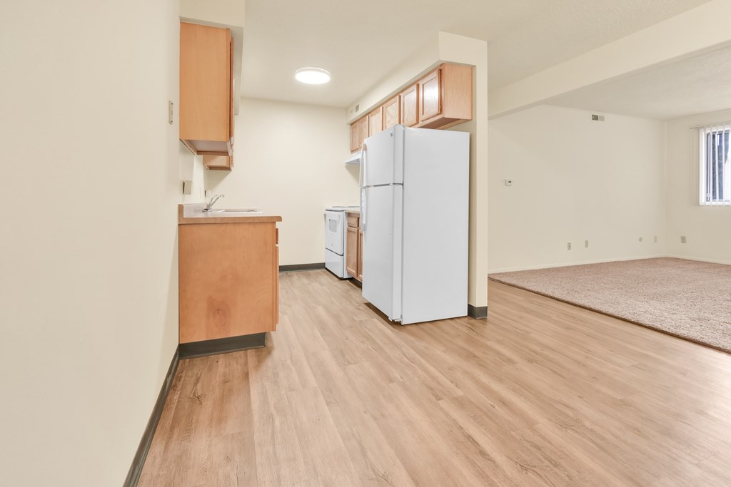 A kitchen with a white fridge and wooden floors.
