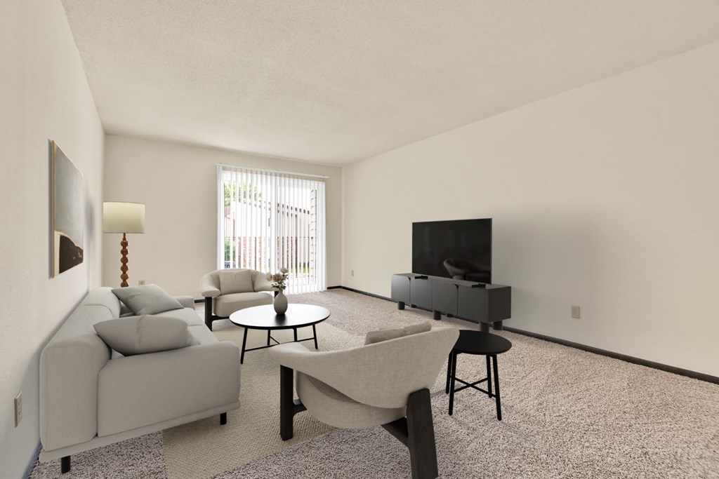 A living room with a grey couch, a black chair, a white chair, a round table, a flat screen TV and a carpet.
