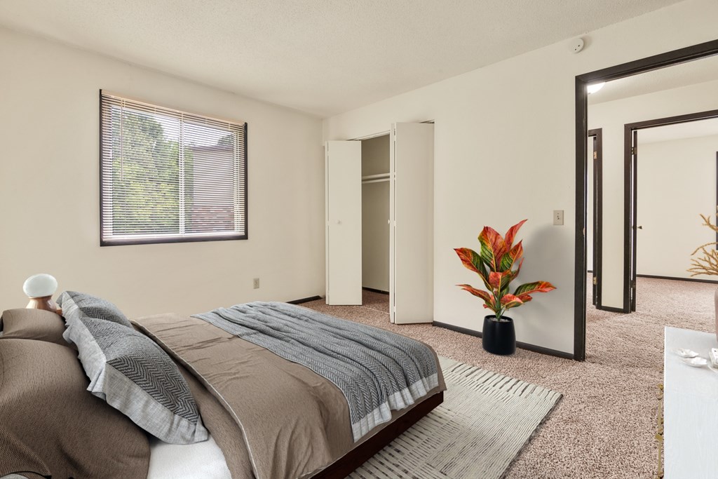 A bedroom with a bed, a potted plant, and a window.