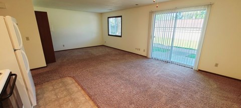 A large empty room with a carpeted floor and a sliding glass door leading outside at Windsor Crest Apartments, Iowa