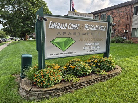 A sign for Emerald Court and Westgate Villa Apartments is surrounded by flowers.