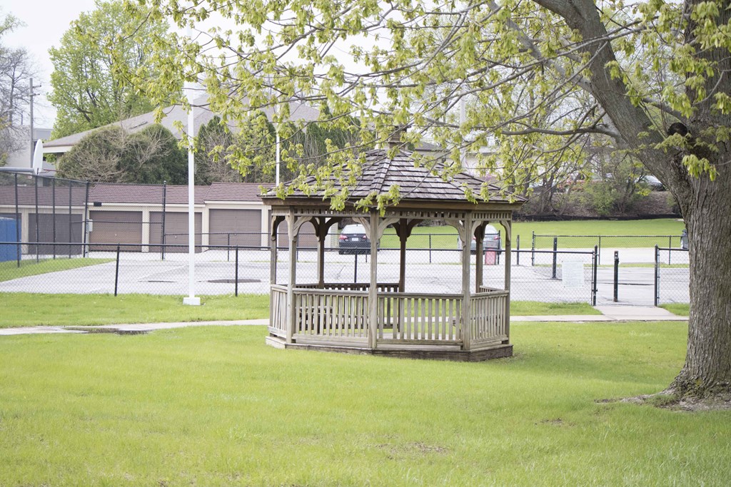 A wooden gazebo sits in a grassy field.