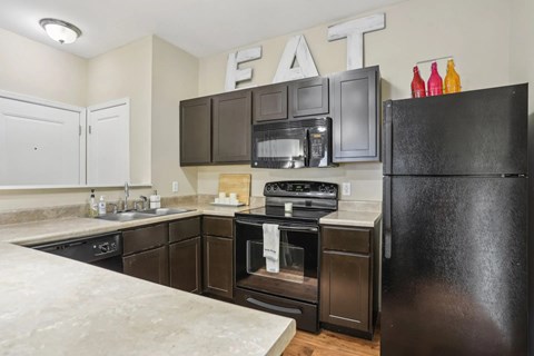 A kitchen with a black fridge and brown cabinets.