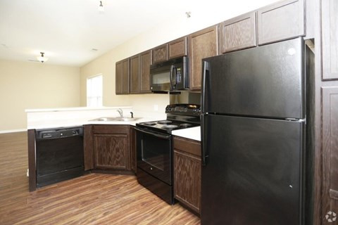 A black refrigerator is in a kitchen with wooden cabinets.