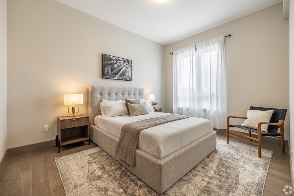A bedroom with a large bed, a chair, and a painting on the wall.