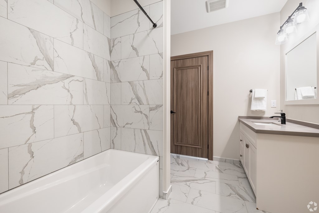 A white marble bathroom with a wooden door.