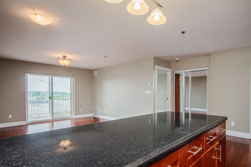 the view from the kitchen of an empty living room with a black counter top and