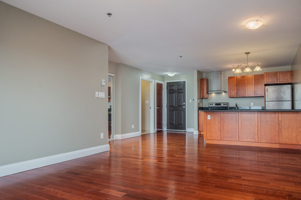 an empty living room with wooden floors and a kitchen