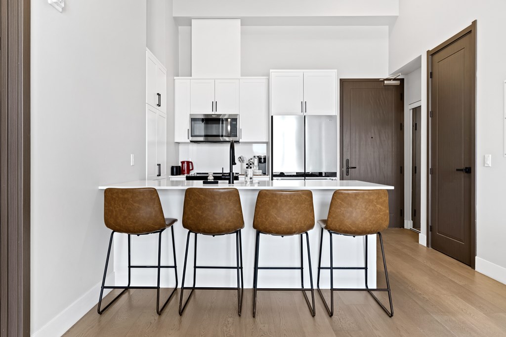 A kitchen with white cabinets and a bar area with brown chairs at The Woods at 180 Kanata Avenue, Kanata, Ontario