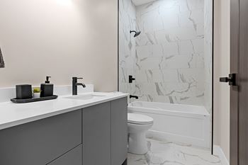 A white toilet sits in a bathroom with a marble wall at The Woods at 180 Kanata Avenue, Kanata, K2K 3L9