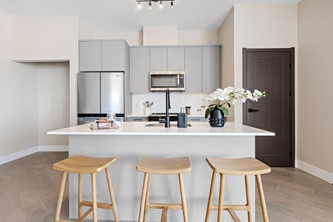 A kitchen with a white counter and bar stools aat The Woods at 180 Kanata Avenue Apartments, Ontario, K2T 0T4