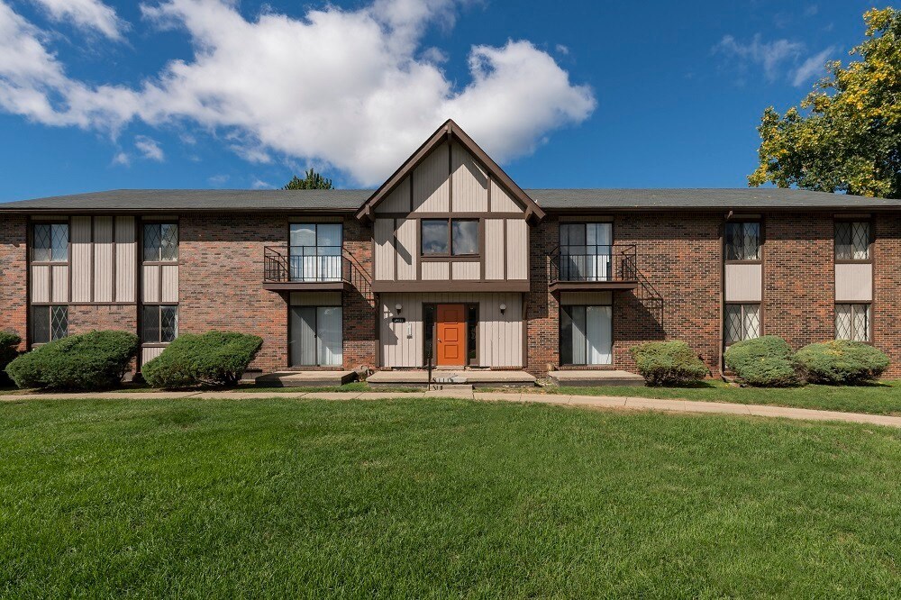 a brick apartment building with a orange door and a green lawn