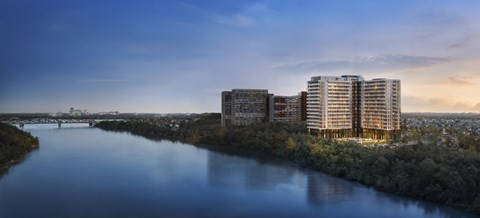 A modern building complex is situated by a river with a bridge in the background.