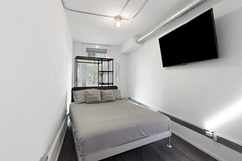 A bedroom with a bed, a window, and a flat screen TV mounted on the wall.