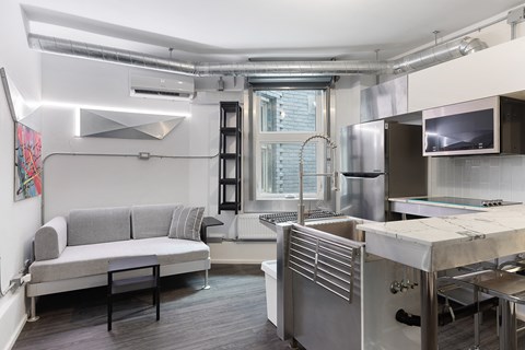 A kitchen with a grey couch and stainless steel appliances.