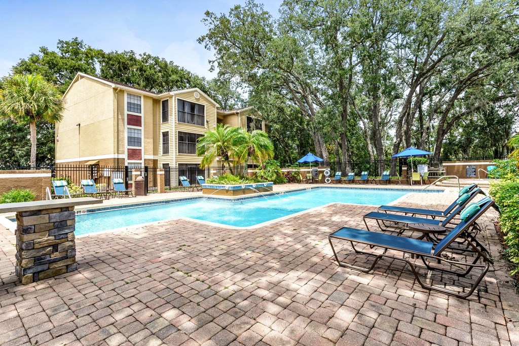 A swimming pool surrounded by a brick patio and lounge chairs.