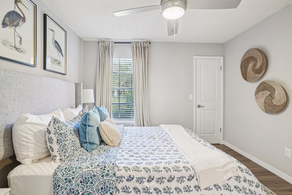 A bedroom with a bed, pillows, a ceiling fan, and a window with curtains.