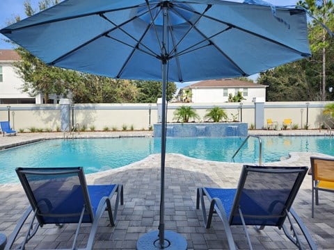 a swimming pool with a blue umbrella and two chairs