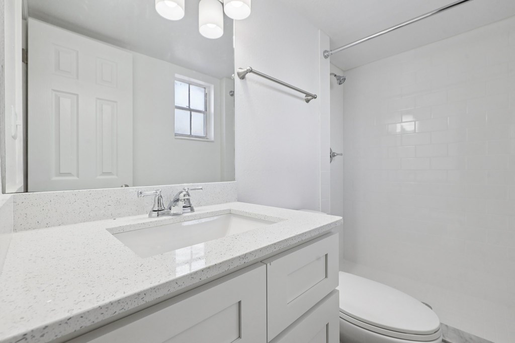 A white bathroom with a sink, toilet, and shower.