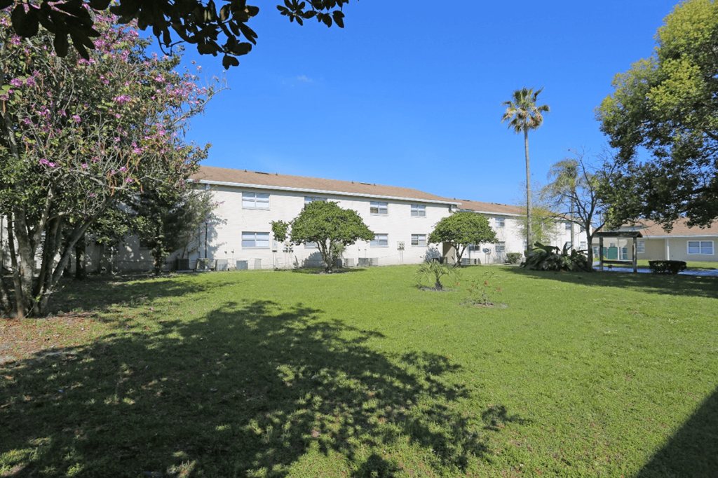 A building is behind a green lawn with a tree and bushes in front.