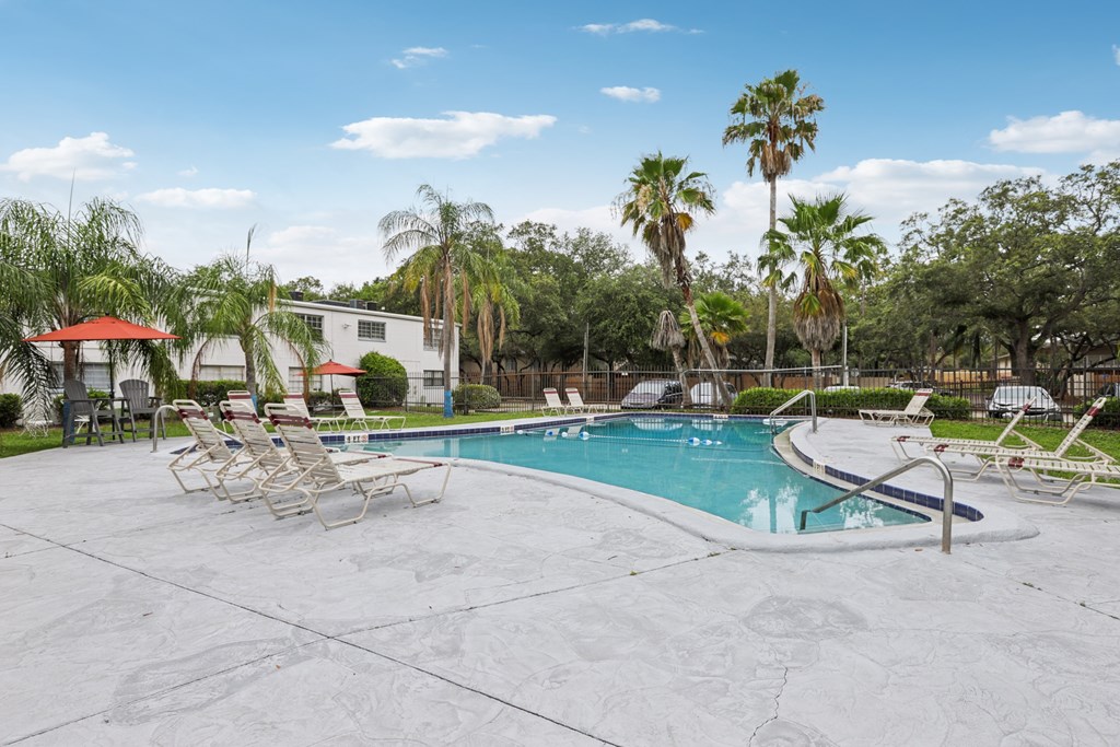 A pool surrounded by palm trees and lounge chairs.