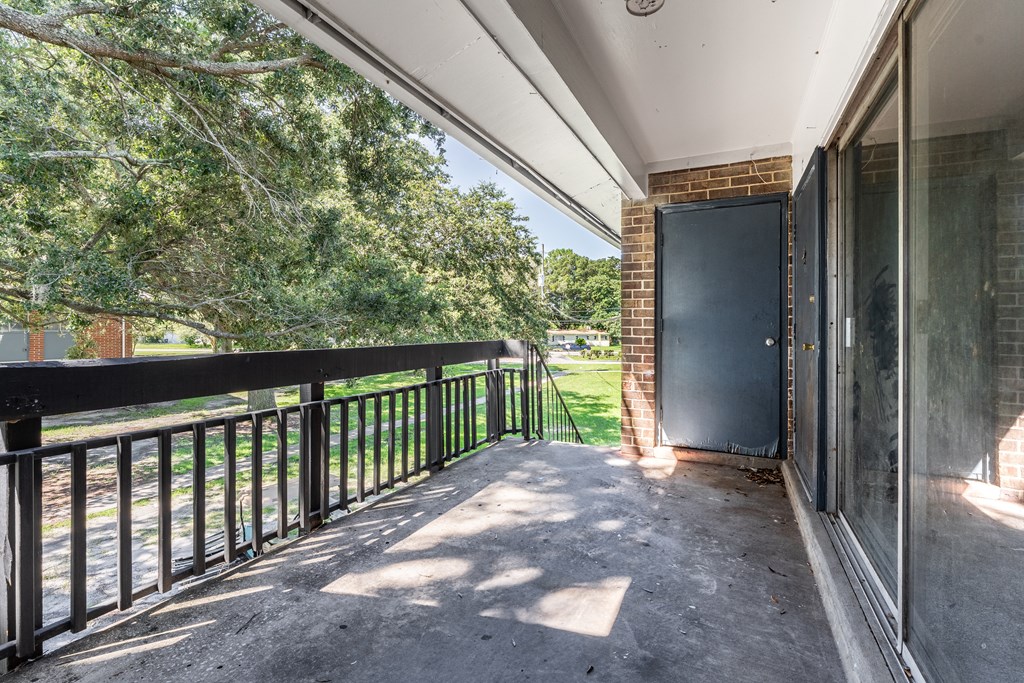 A balcony with a black railing and a view of trees and a brick building.