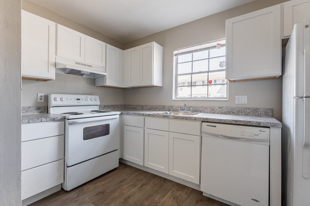 A white kitchen with a stove, oven, dishwasher, and refrigerator.