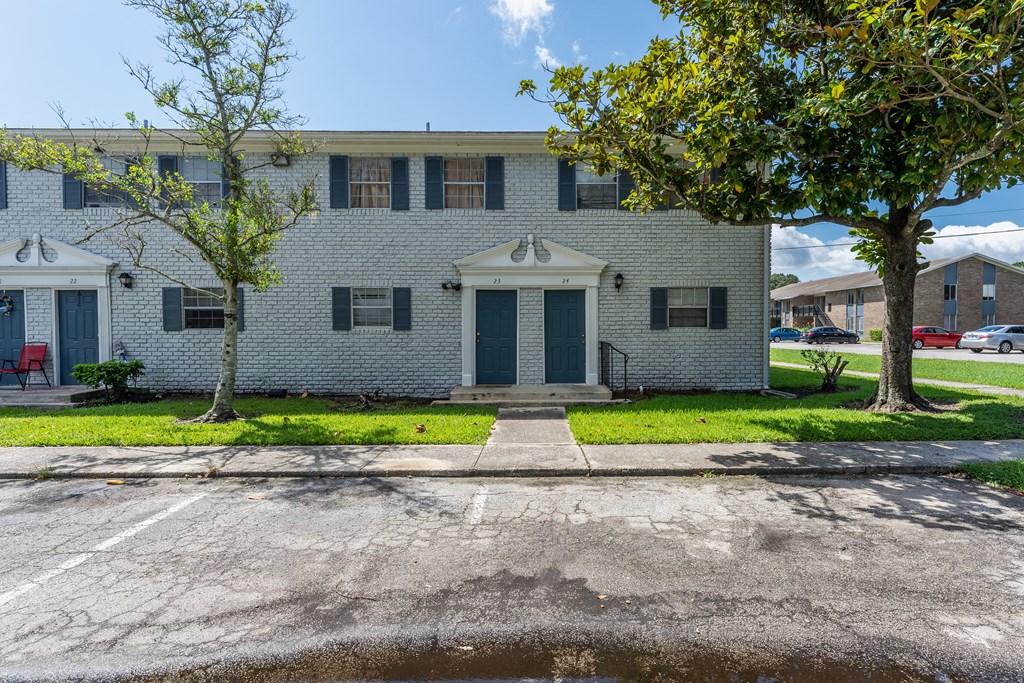A grey building with a red door and a tree in front.