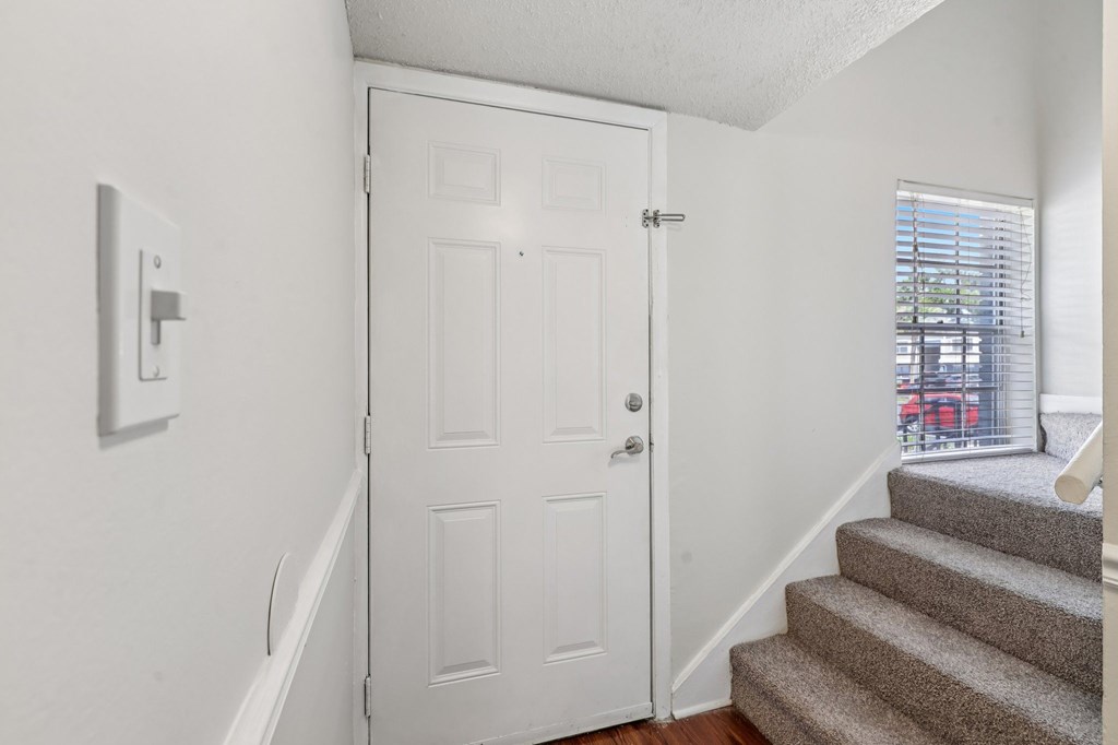A white door is in a hallway with a staircase.