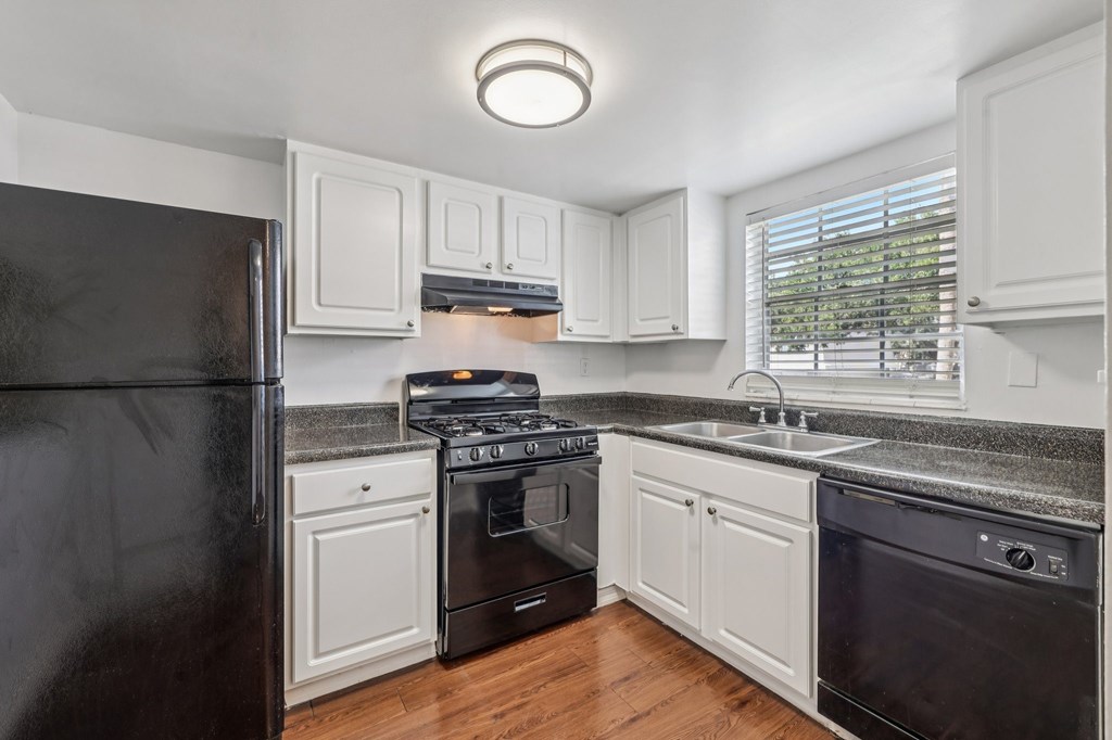 A black refrigerator is in a kitchen with white cabinets.