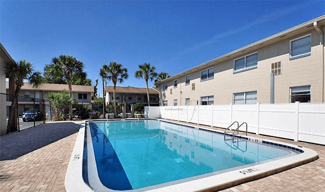 A swimming pool in front of a building with a white fence.