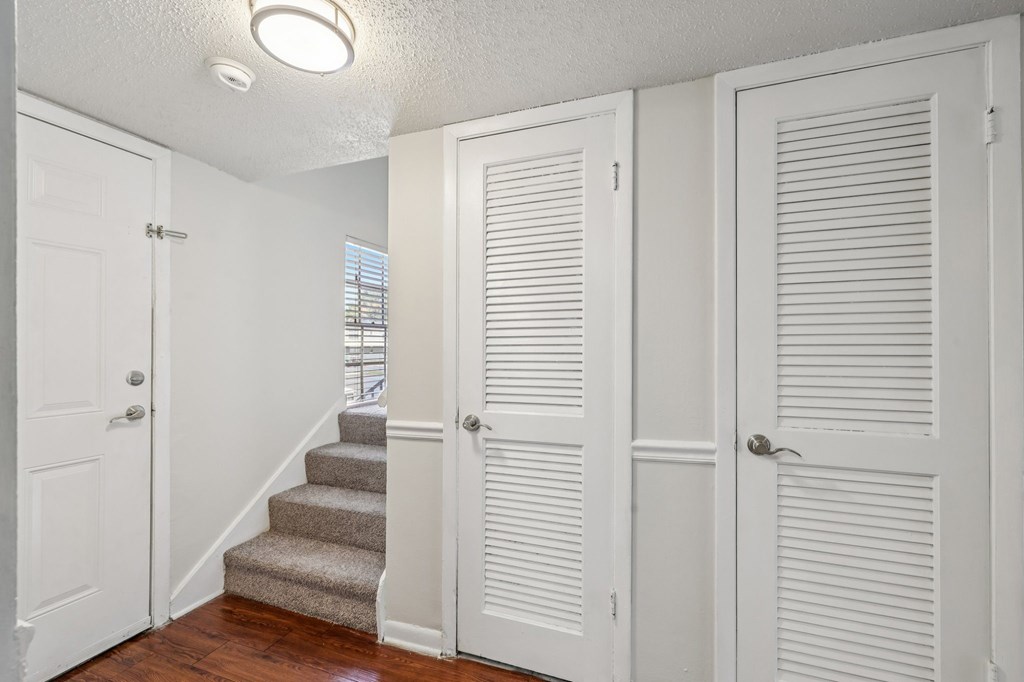 A white door is on the left of a hallway with a staircase.