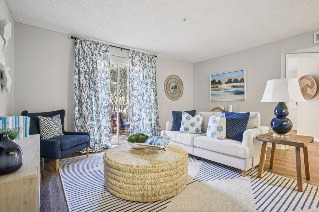 A living room with a white couch, a round wicker table, and a painting on the wall.