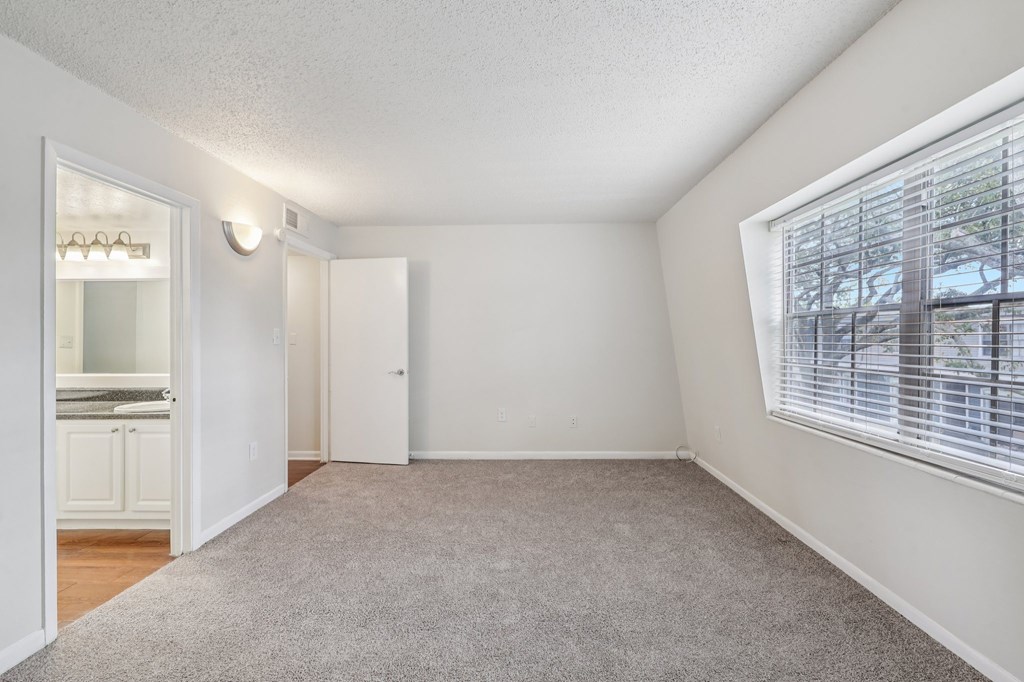 A room with a carpeted floor and a window with blinds.