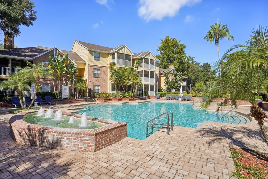 A pool with a fountain in the middle of a brick patio.