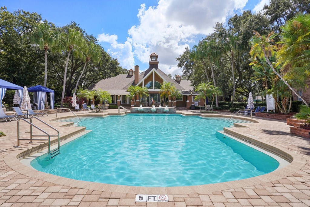 A large swimming pool surrounded by a brick patio and a gazebo in the background.