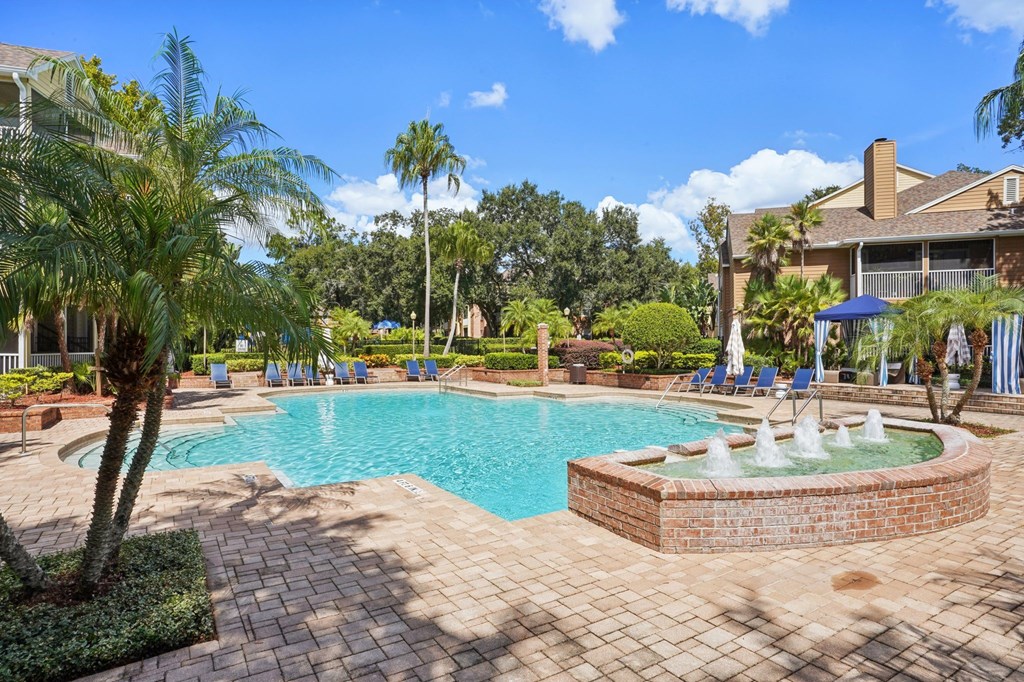 A pool with a fountain in the middle of a brick patio.