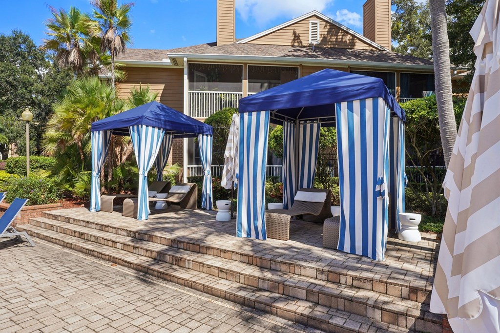 Two blue and white striped canopies are set up on a brick patio.