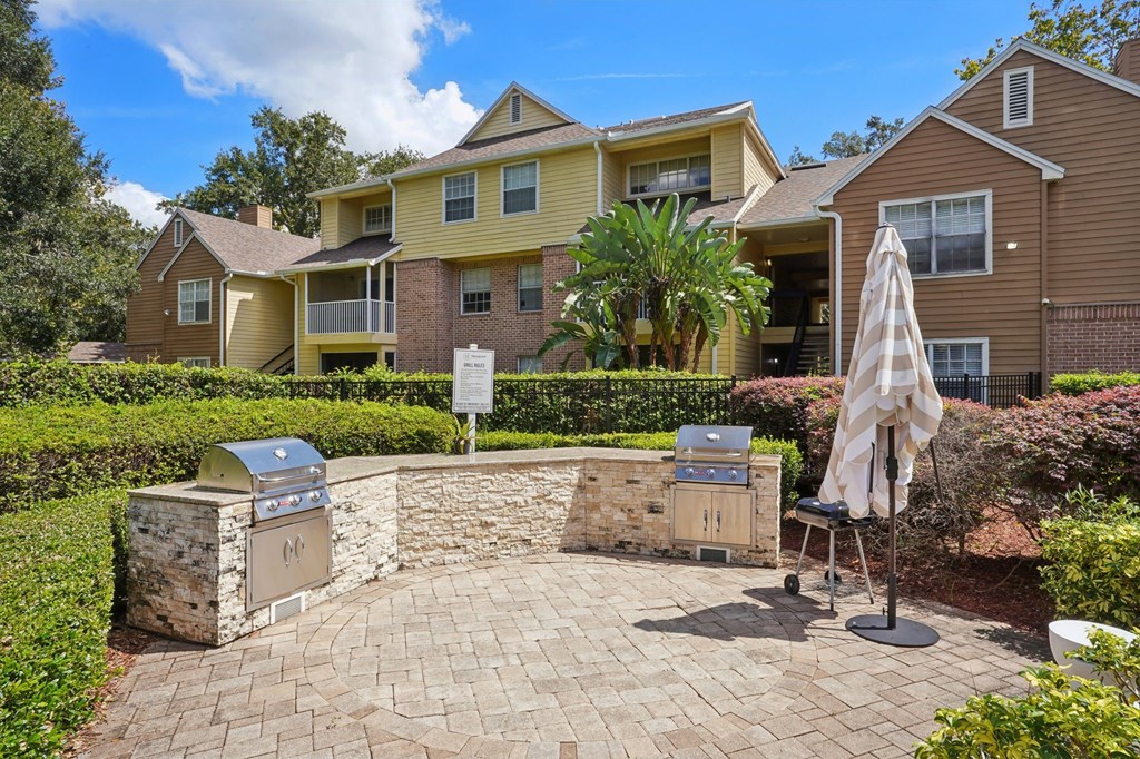 A patio with a grill and umbrella in front of a house.