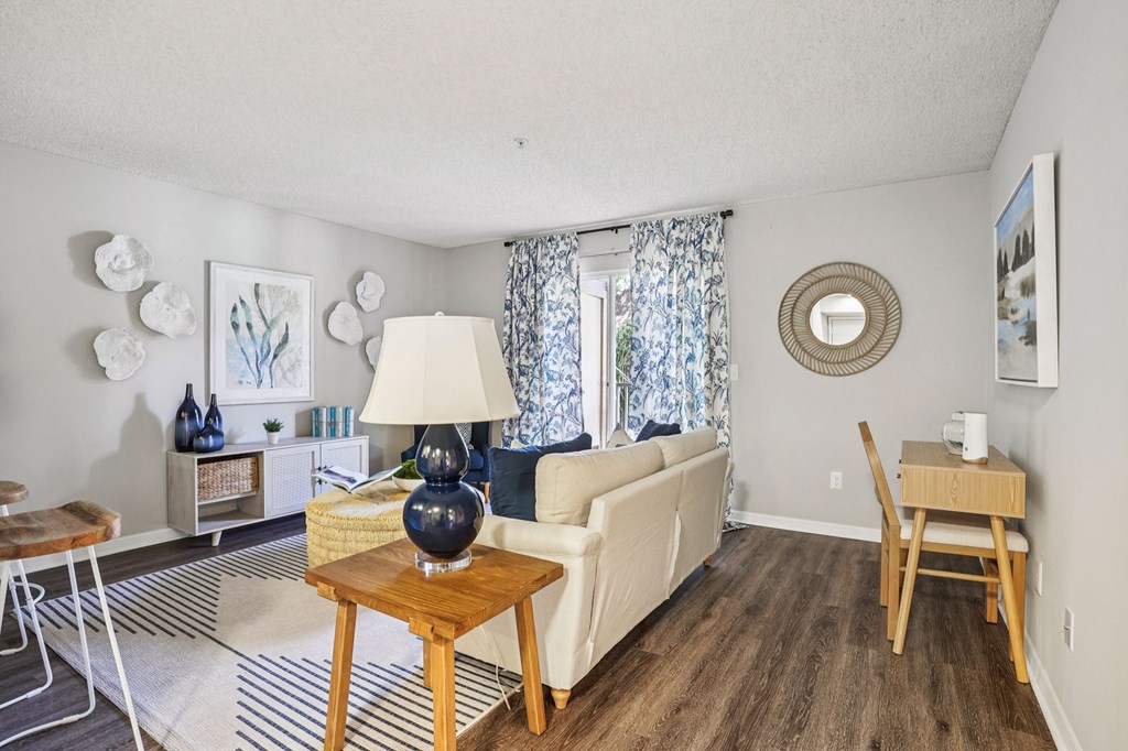 A living room with a white couch, a wooden coffee table, and a round mirror on the wall.