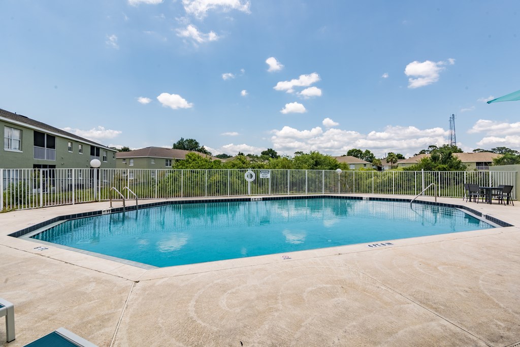A swimming pool surrounded by a concrete patio and a metal fence.