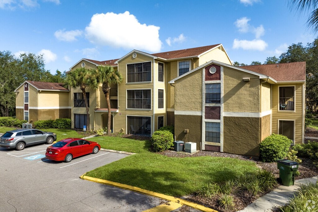 A red car is parked in a parking lot in front of a building.