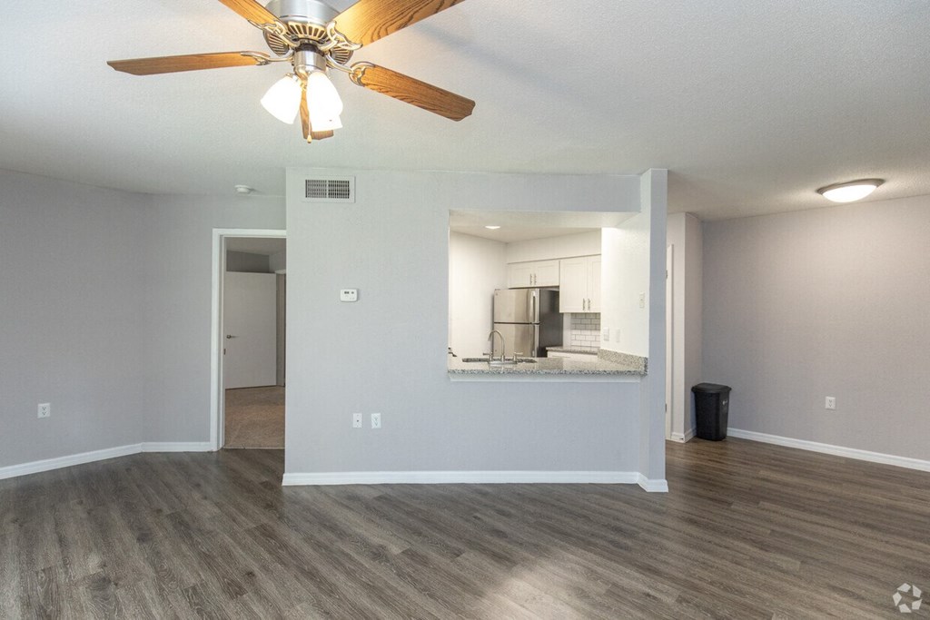 A room with a ceiling fan and a kitchenette in the background.