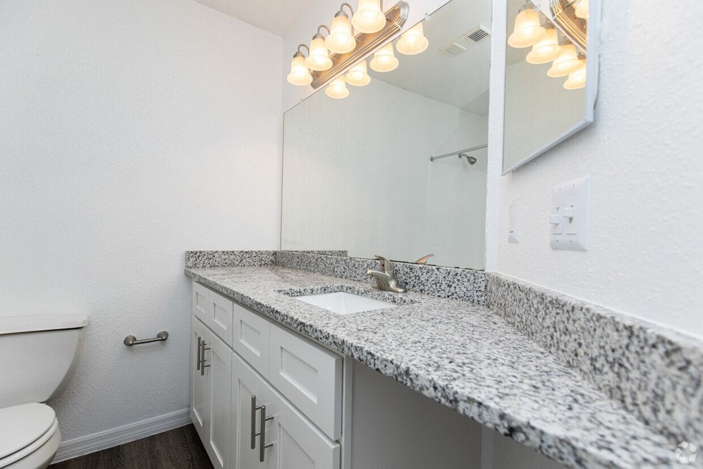 A bathroom with a granite countertop and a mirror with lights above it.