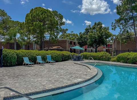 A swimming pool surrounded by a brick patio and lawn chairs.