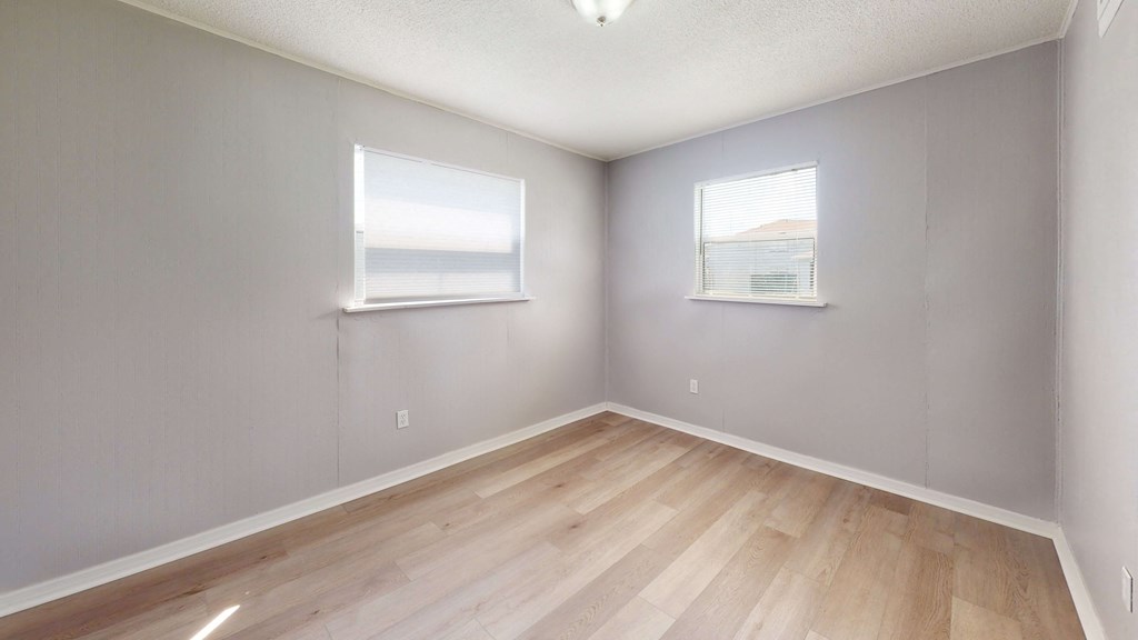a bedroom with two windows and a hardwood floor