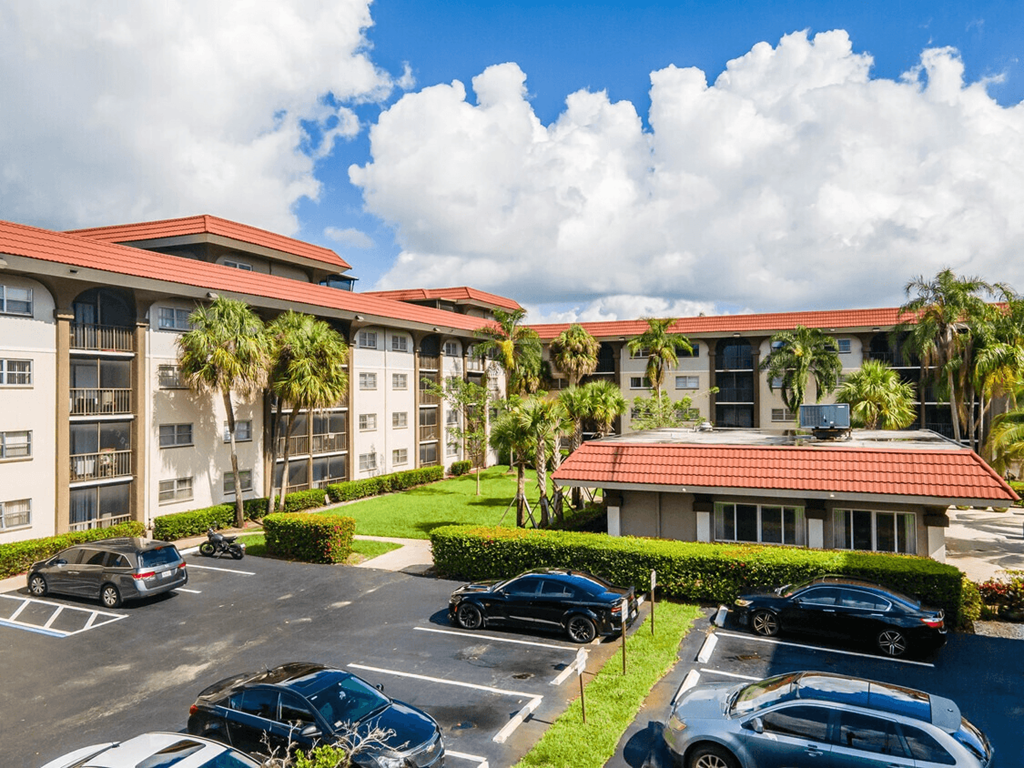 A parking lot with cars and a building with palm trees in front.